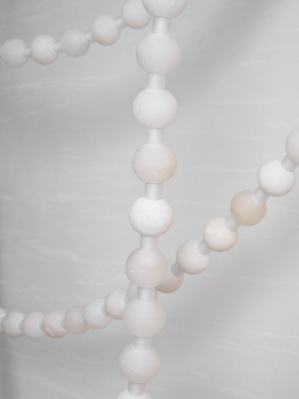 Close-up of a lit alabaster strand on the Clérachic chandelier, with a second strand and gold mounts soft-focused behind.