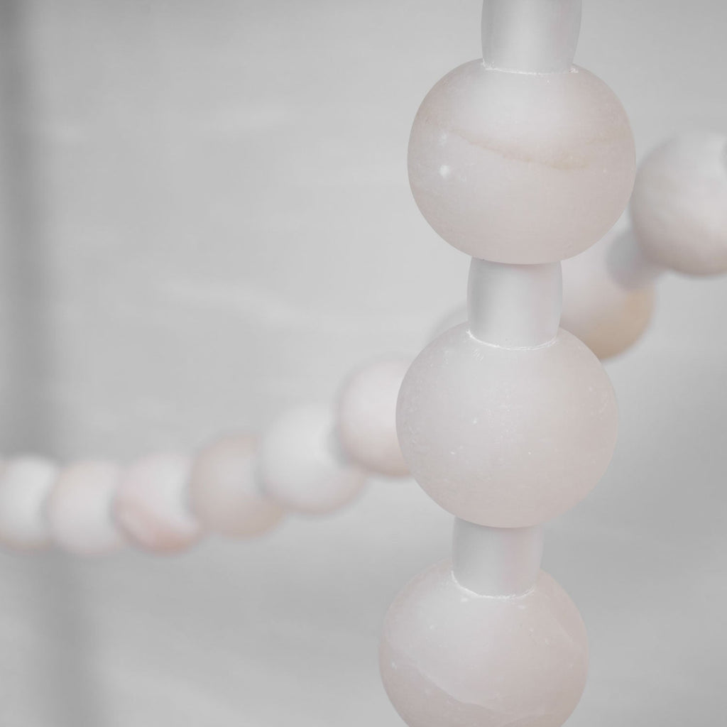 Macro shot of the Clérachic alabaster bead chandelier's LED glowing warmly through the stone beads along the strand.
