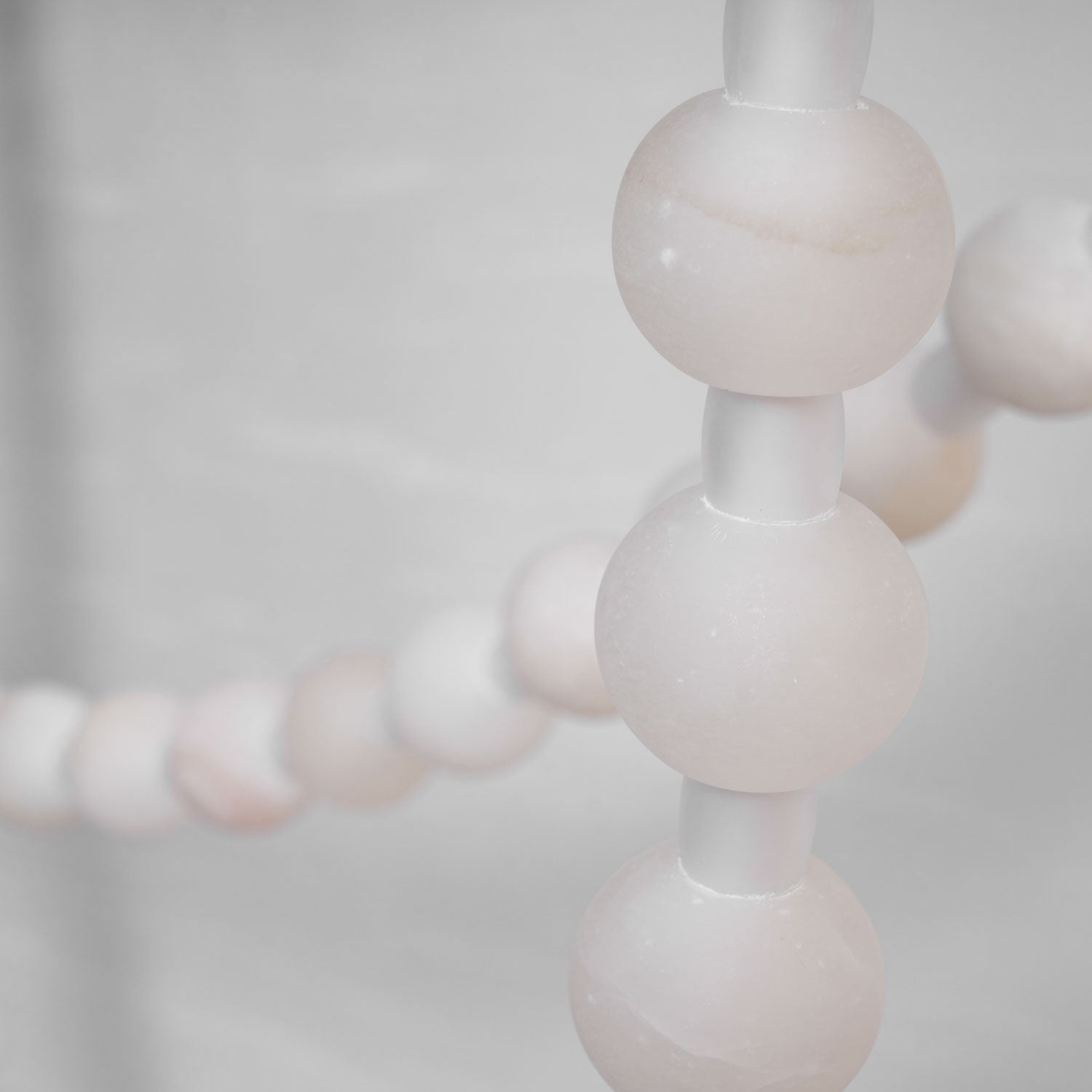 Macro shot of the Clérachic alabaster bead chandelier's LED glowing warmly through the stone beads along the strand.
