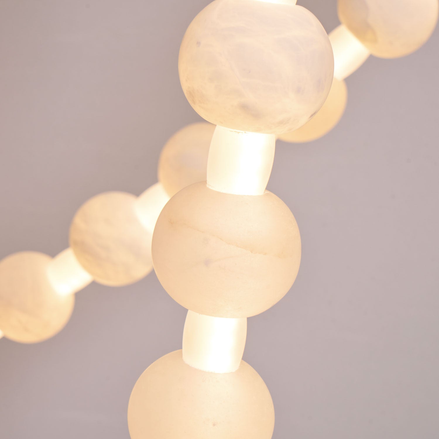 Warm light glows through stacked alabaster beads on the Clérachic chandelier in this close macro detail.