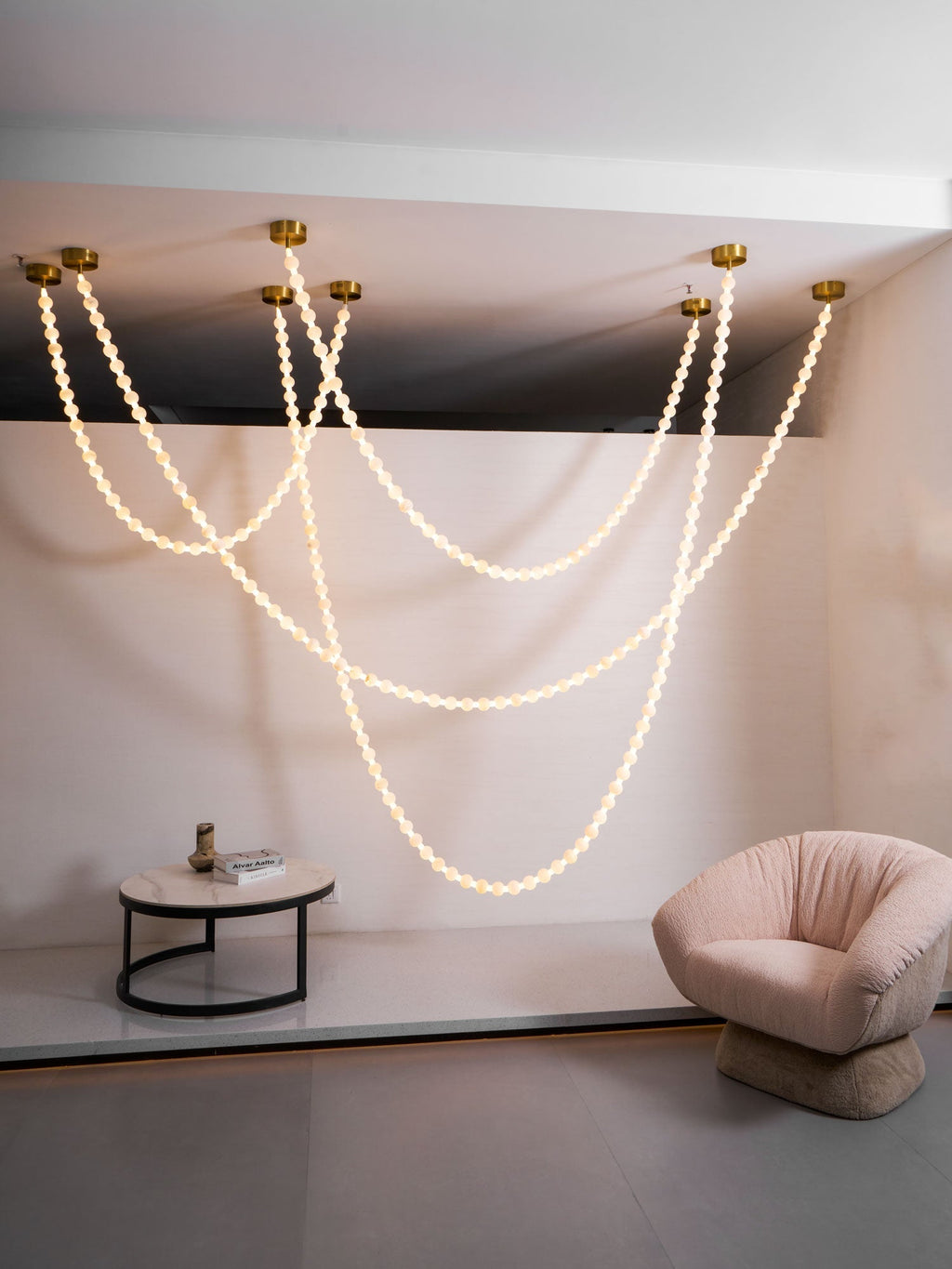 The Clérachic alabaster bead chandelier's four-strand cascade lit above a stairwell landing, beside a blush armchair and marble side table.