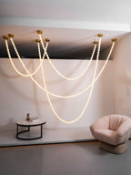 The Clérachic alabaster bead chandelier's four-strand cascade lit above a stairwell landing, beside a blush armchair and marble side table.