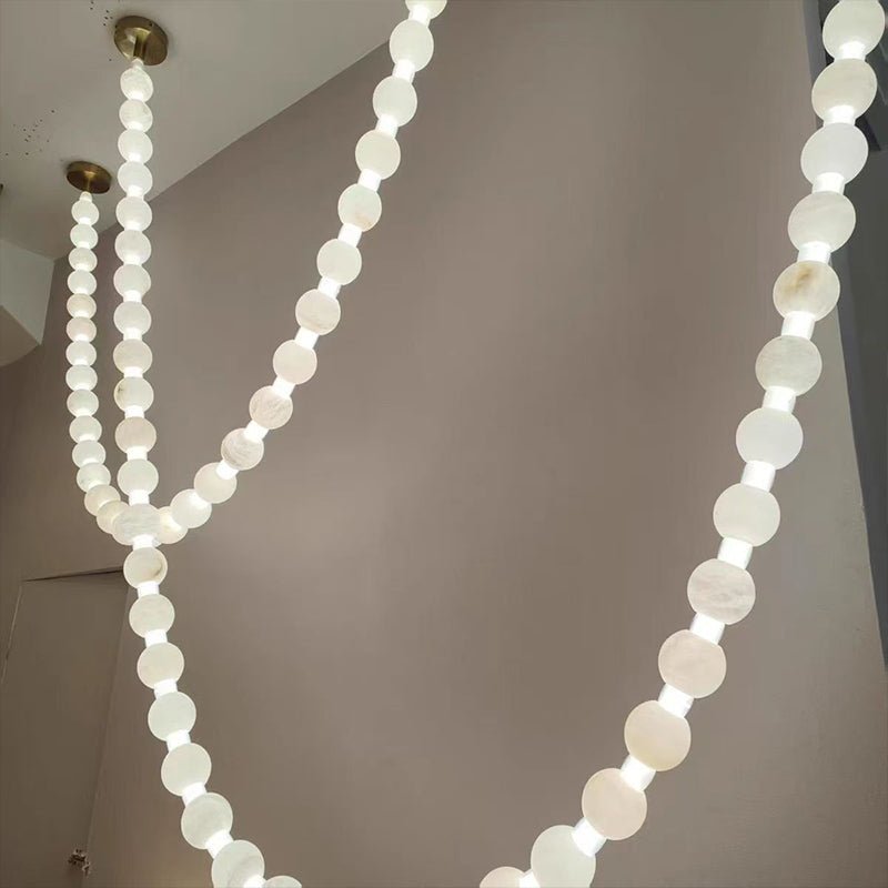 Two crossing strands of the Clérachic alabaster bead chandelier glow warmly from gold ceiling mounts above a lounge area.