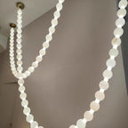 Two crossing strands of the Clérachic alabaster bead chandelier glow warmly from gold ceiling mounts above a lounge area.