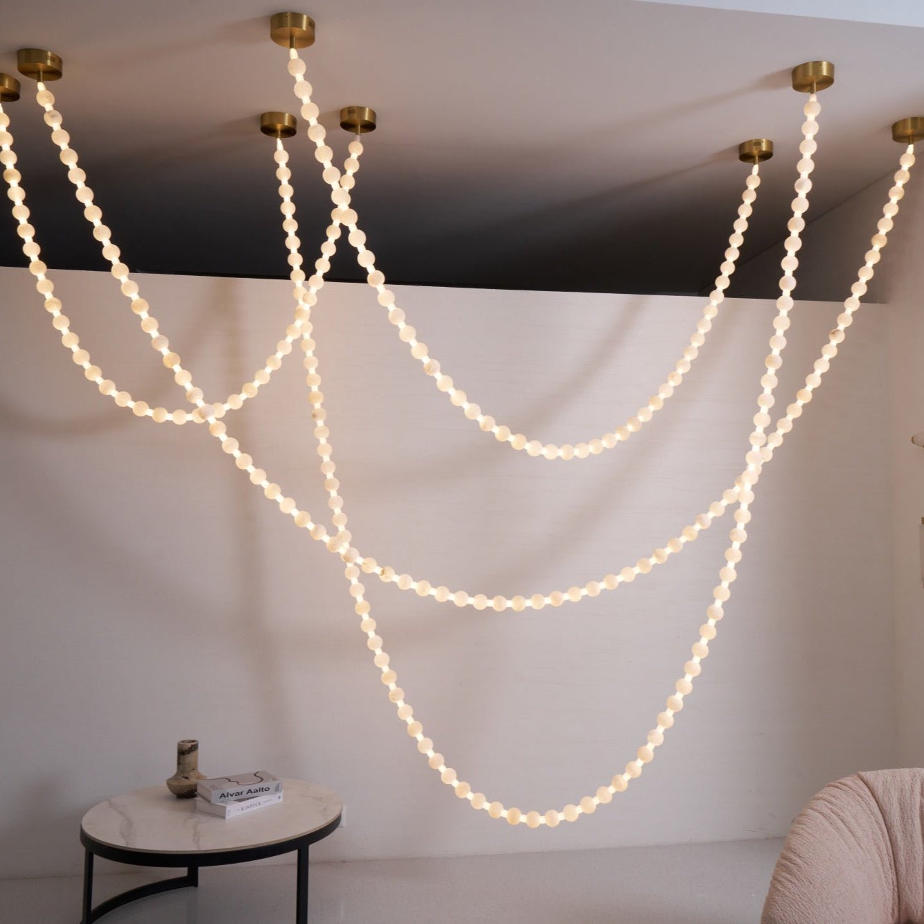 Wide view of the Clérachic alabaster bead chandelier's cascading strands lit above a living space with a blush chair and coffee table.
