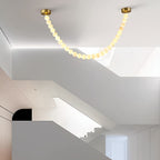The Clérachic alabaster bead chandelier's single strand spans a sloped ceiling above an open stairwell landing.