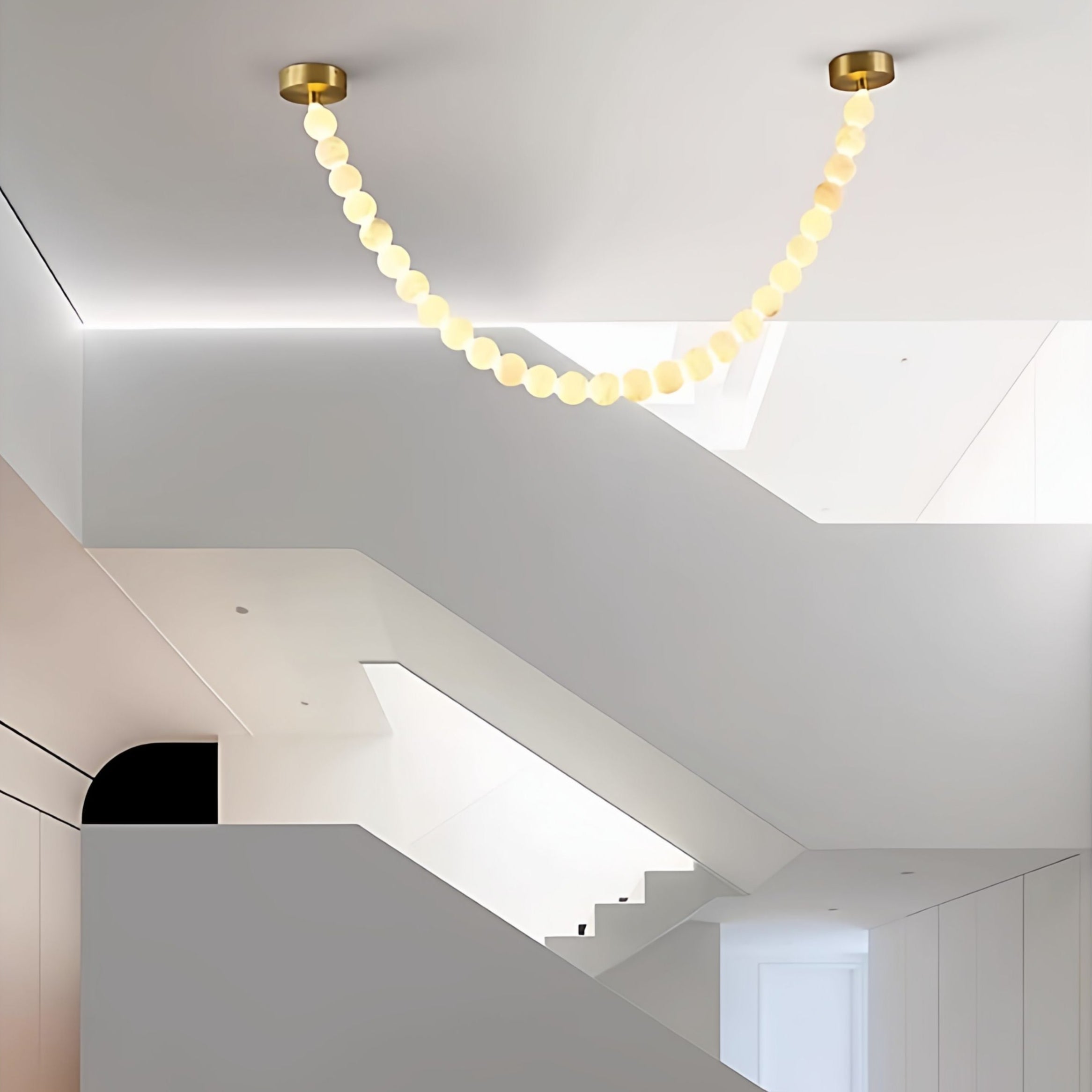 The Clérachic alabaster bead chandelier's single strand spans a sloped ceiling above an open stairwell landing.