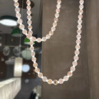 The Clérachic alabaster bead chandelier hangs in a showroom setting, reflected beside pendant lamps in the background.