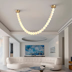 The Clérachic alabaster bead chandelier's single strand glows above a white sofa and blue abstract artwork in a living room.