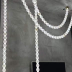 Multiple lit strands of the Clérachic alabaster bead chandelier hang against a concrete wall near a wall-mounted screen.