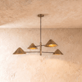 Clérachic linear chandelier in aged vintage brass, four cone shades branching from crossed arms below a plaster ceiling.