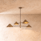 Clérachic linear chandelier in aged vintage brass, four cone shades branching from crossed arms below a plaster ceiling.