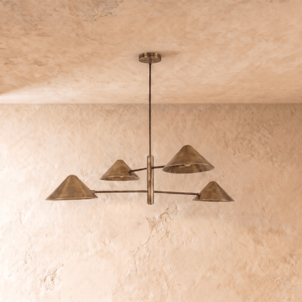 Clérachic four-arm linear chandelier in vintage brass, cone shades angled outward under a softly textured ceiling.