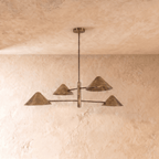 Clérachic four-arm linear chandelier in vintage brass, cone shades angled outward under a softly textured ceiling.