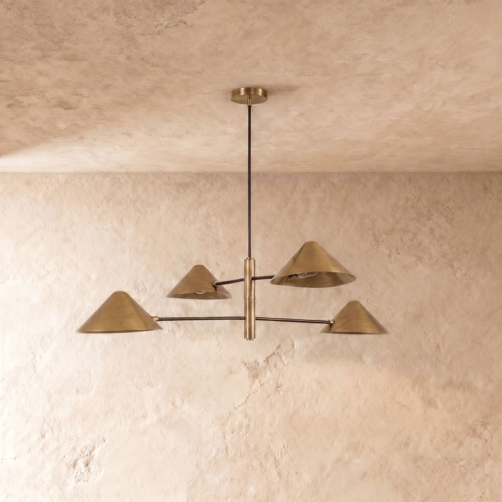 Clérachic four-light linear chandelier in satin brass, cone shades glowing warm against a plaster ceiling.