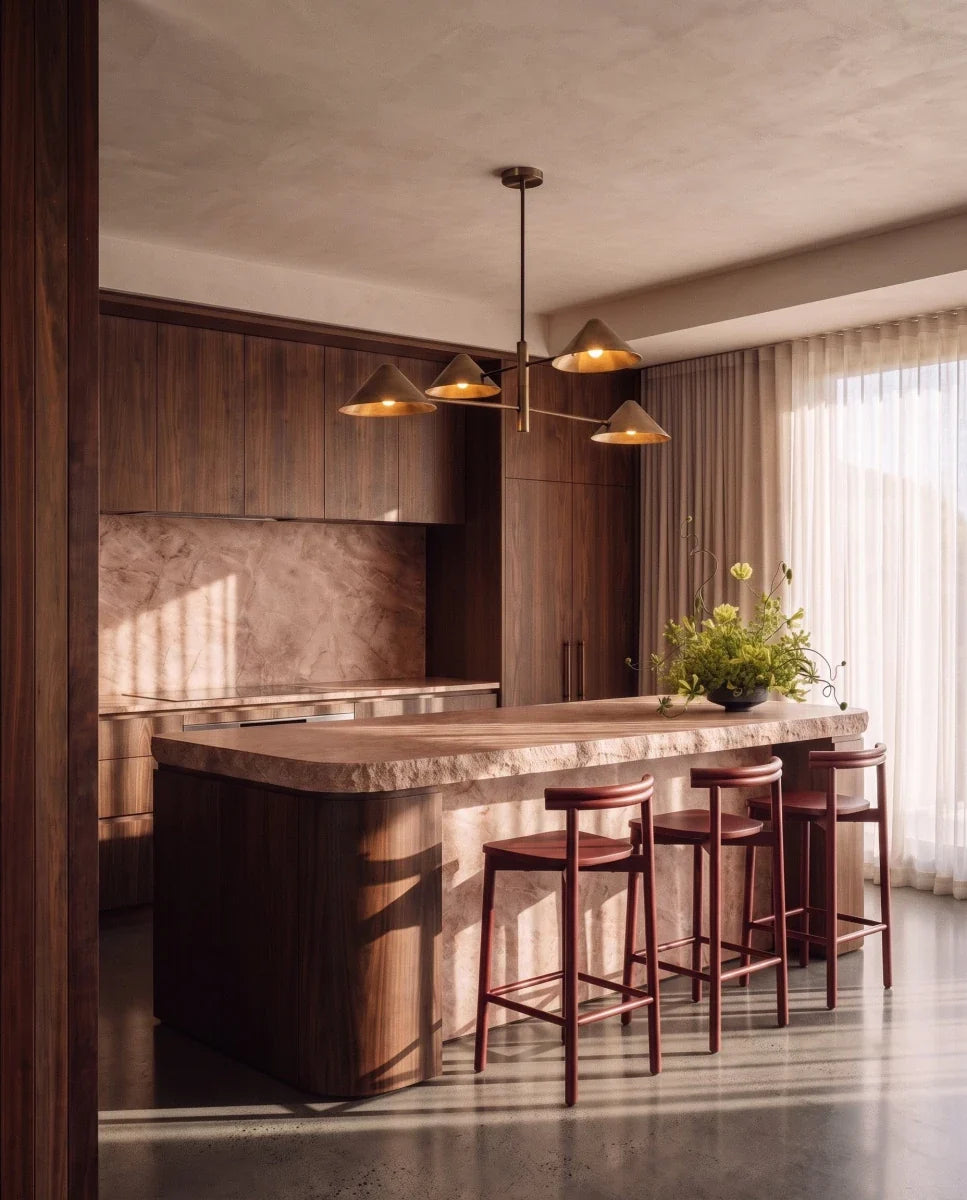 Clérachic linear chandelier in brass hanging over a stone kitchen island with walnut cabinetry and bar stools.