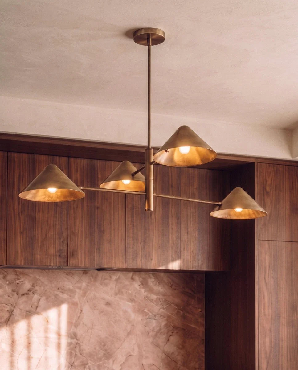 Clérachic linear chandelier in brass glowing above walnut kitchen cabinetry beside a marble-look backsplash.