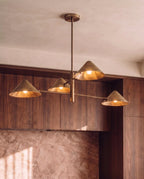 Clérachic linear chandelier in brass glowing above walnut kitchen cabinetry beside a marble-look backsplash.