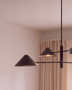 Clérachic linear chandelier detail in matte black, cone shades and crossed arms shown against a curtained window.