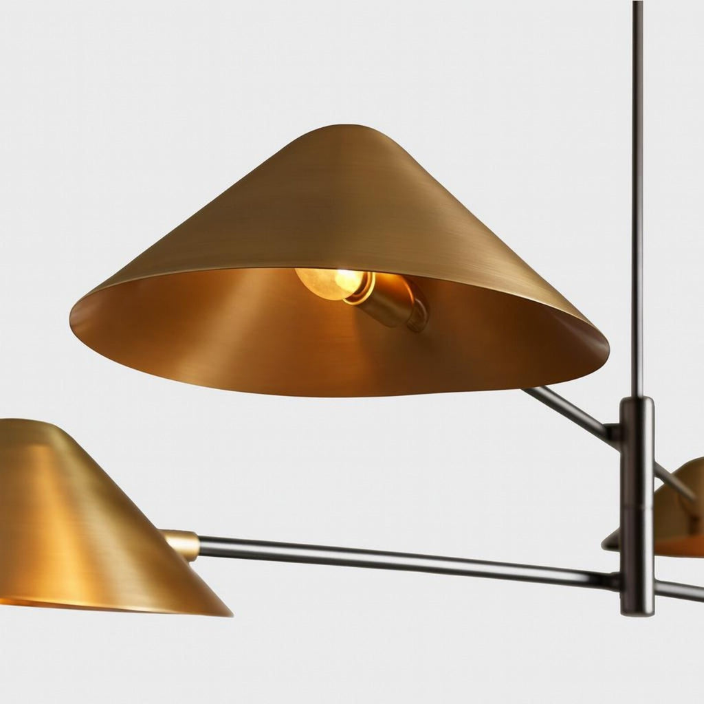 Close view of a Clérachic brushed brass cone shade glowing around its bulb, with the dark metal arm and centre stem