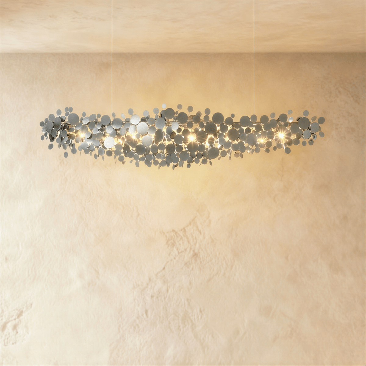 Clérachic linear chandelier of polished chrome discs on two fine cables, lit warm against a soft limewash wall.