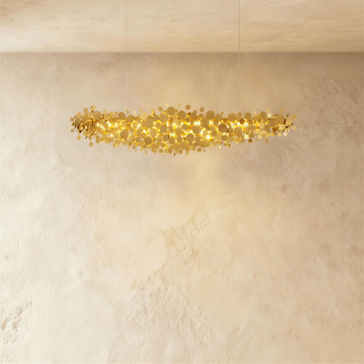 Clérachic shorter gold disc chandelier suspended on two thin cables, its warm light spilling over a textured plaster wall.