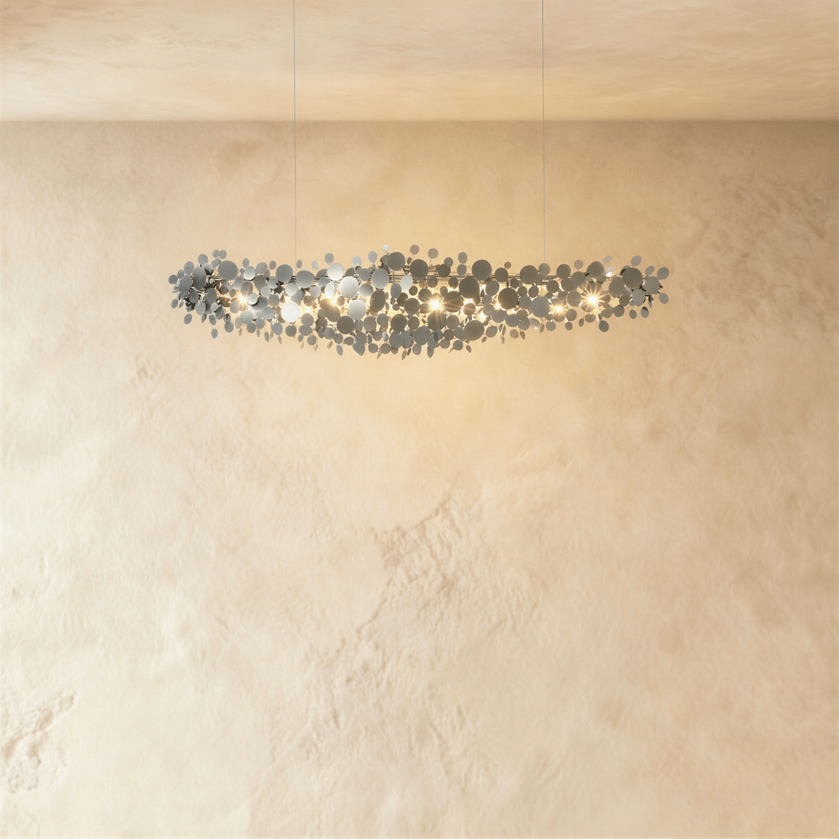 Clérachic compact chrome disc chandelier on two thin cables, glowing against a cream plaster wall.