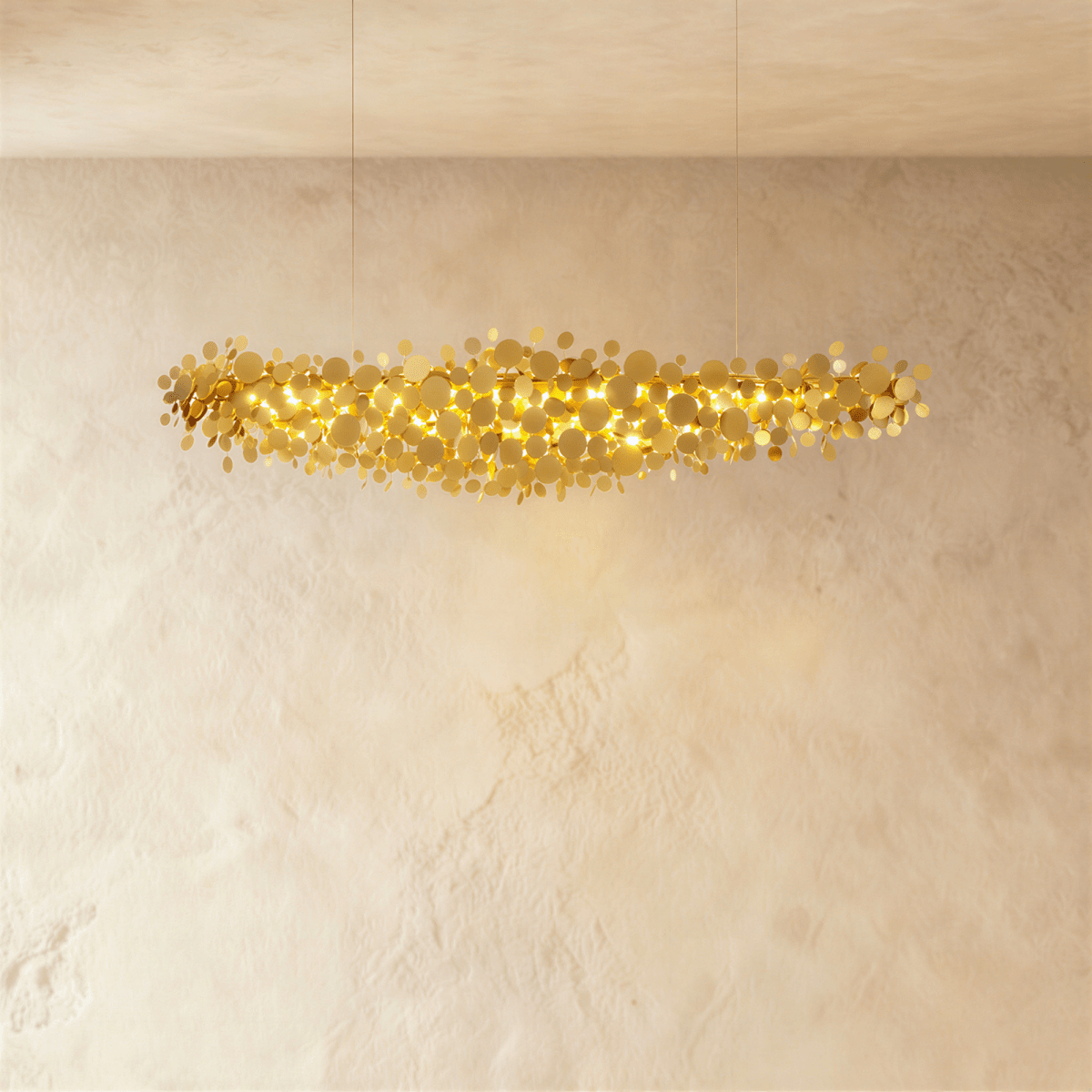 Clérachic mid-length gold disc chandelier with a cloud of overlapping metal discs lit from within, on a limewash wall.
