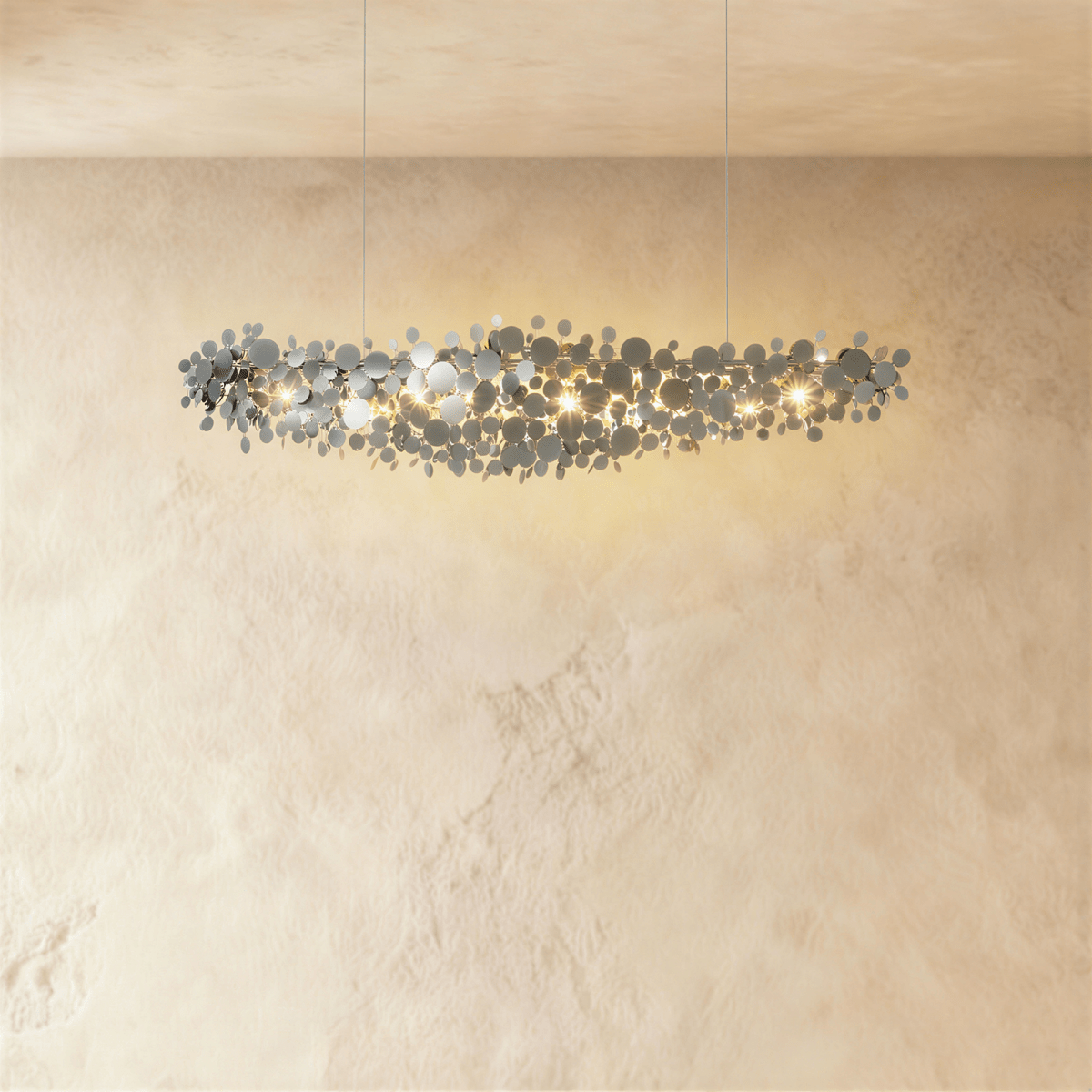 Clérachic mid-length chrome disc chandelier, its overlapping mirrored discs catching warm light on a plaster wall.