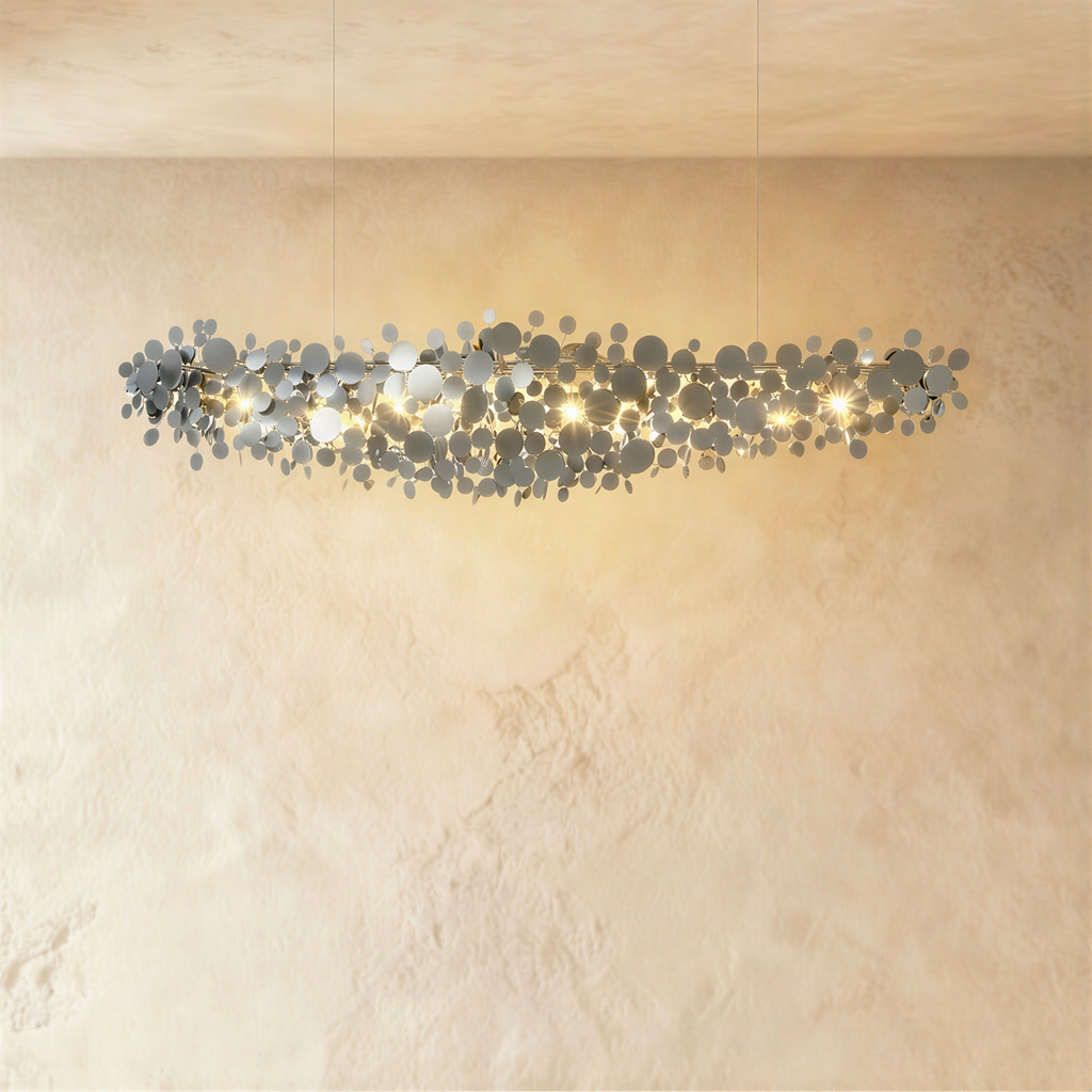 Clérachic long chrome disc chandelier, mirrored metal discs sparkling with warm light on a cream wall.