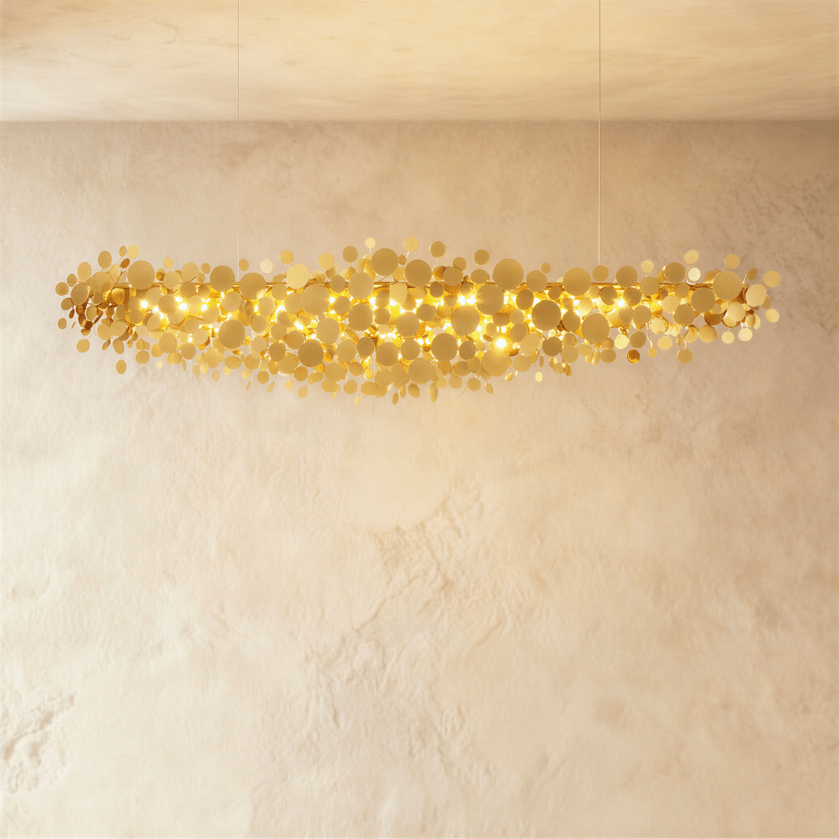 Clérachic longest gold disc chandelier spanning the frame, hundreds of metal discs glowing warm against limewash.