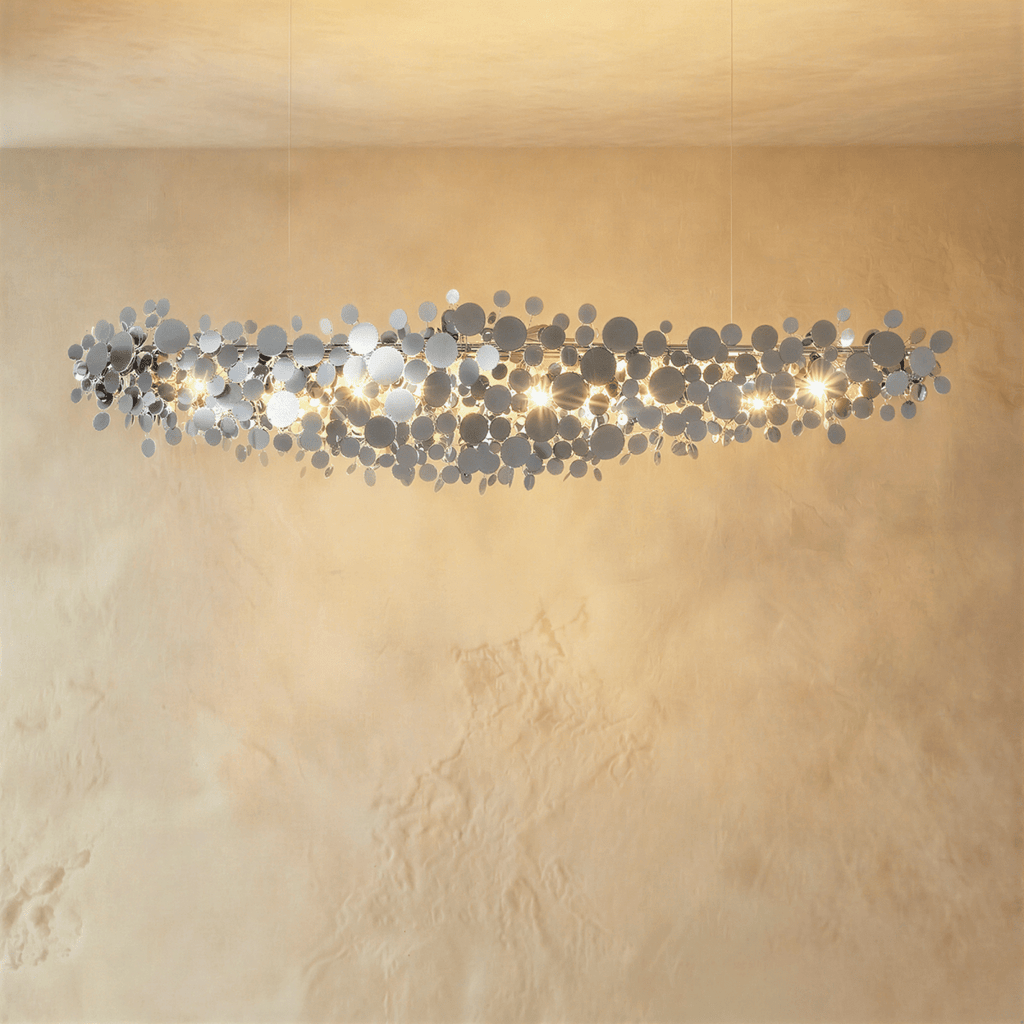 Clérachic longest chrome disc chandelier, a wide cloud of mirrored discs lit warm against a plaster wall.