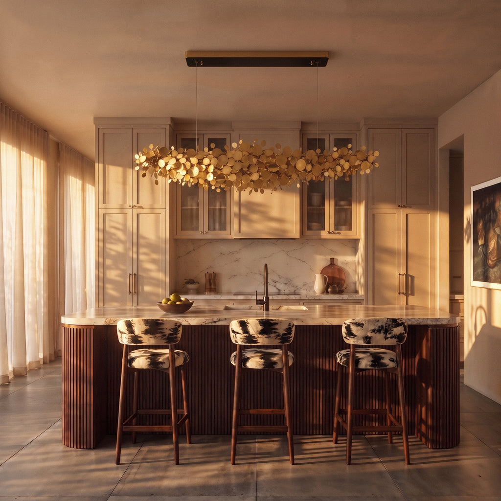 Clérachic gold disc chandelier hung above a marble kitchen island with fluted timber base and three upholstered stools.