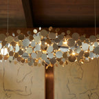 Close detail of the Clérachic chandelier, its round metal discs in mixed gold and silver tones lit by tiny warm bulbs.