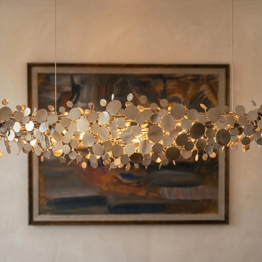 Clérachic chrome disc chandelier seen close up against a framed painting, mirrored discs lit with a soft warm glow.