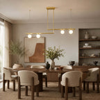Over a round dark dining table with boucle chairs, this Clérachic chandelier carries four frosted globes on two offset brass bars.