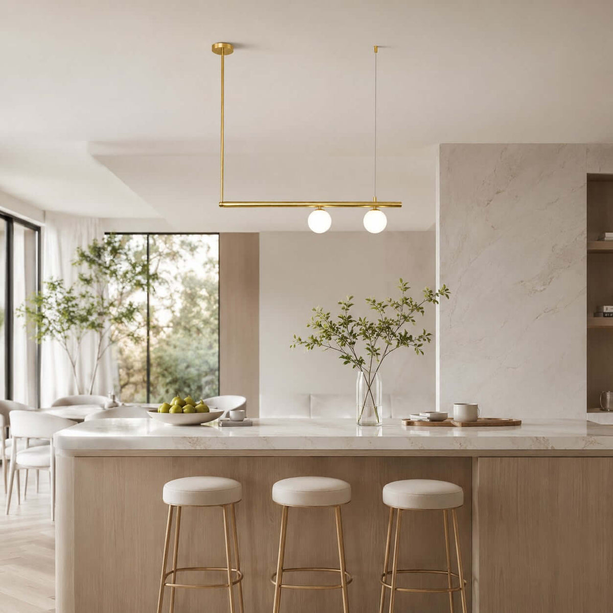 This Clérachic chandelier has one brass bar and two lit frosted globes, above a marble island with brass-legged stools and a bright garden view.
