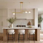 A Clérachic chandelier with one globe on a short bar and two on a longer one hangs above a kitchen island with boucle stools.