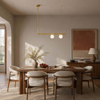 Single-bar Clérachic chandelier with two frosted globes, hung over a wooden dining table in a room with an arched doorway.