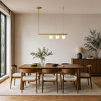This Clérachic brass chandelier carries three lit globes on one bar, over a walnut dining table and a wooden sideboard.