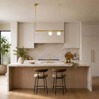 This Clérachic chandelier, with a single brass bar and two lit frosted globes, hangs before white kitchen cabinets above a wood-fronted island.
