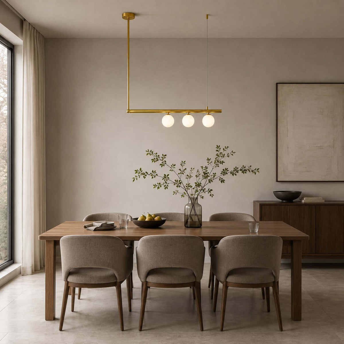 Three lit globes on a single brass bar, from Clérachic, over a dark wood dining table with taupe chairs and a framed canvas behind.