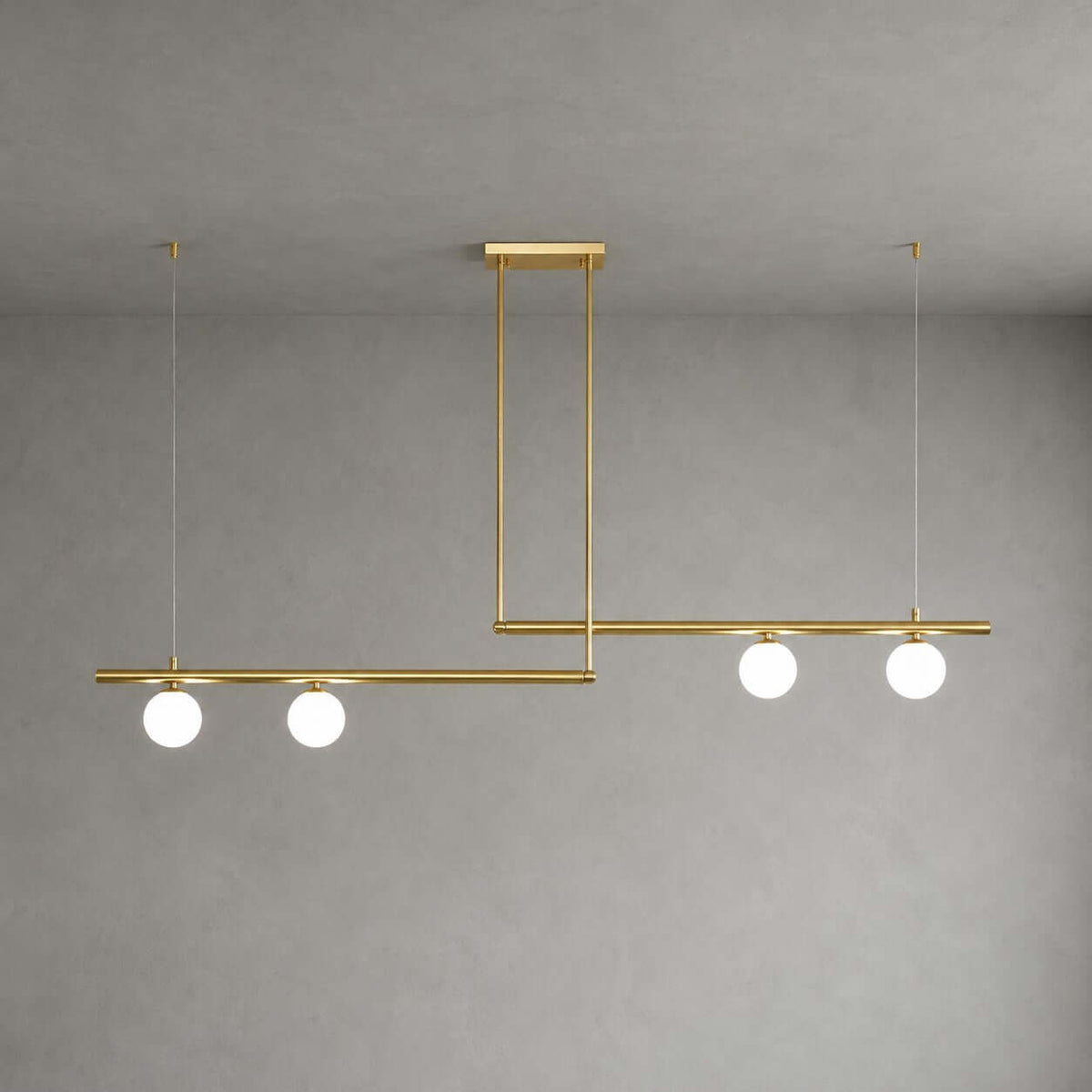 Clérachic linear chandelier with two brass bars, each with two lit frosted globes, hung from a rectangular canopy against a grey wall.