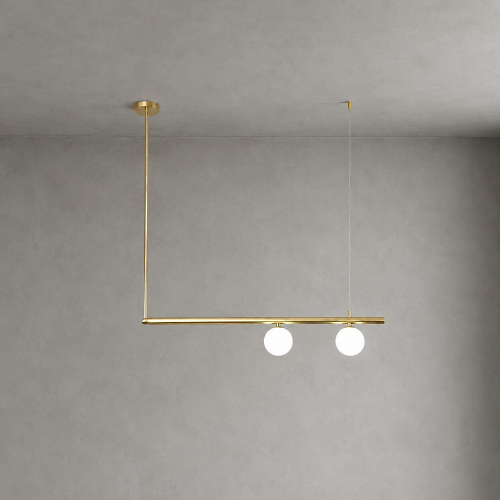 Clérachic chandelier with a single brass bar, two lit frosted globes and an L-shaped drop from a round canopy, on a grey wall.