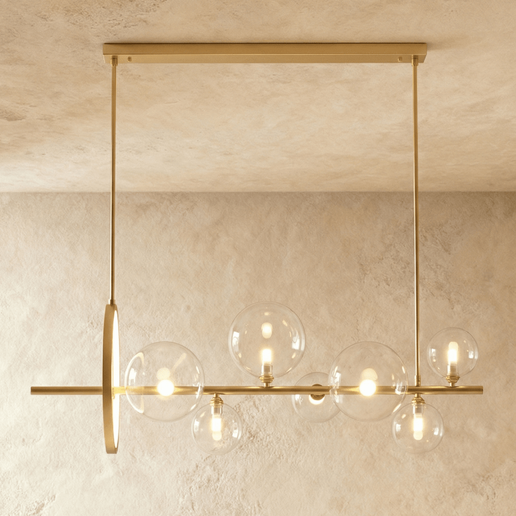 Clérachic gold bar chandelier with seven clear glass globes of mixed sizes and an upright gold ring, hung against limewash.