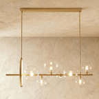 Clérachic gold bar chandelier with seven clear glass globes of mixed sizes and an upright gold ring, hung against limewash.