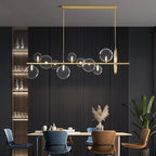 Clérachic gold bar chandelier with clear glass bubble globes above a dining table with blue and tan chairs, dark slatted wall behind.