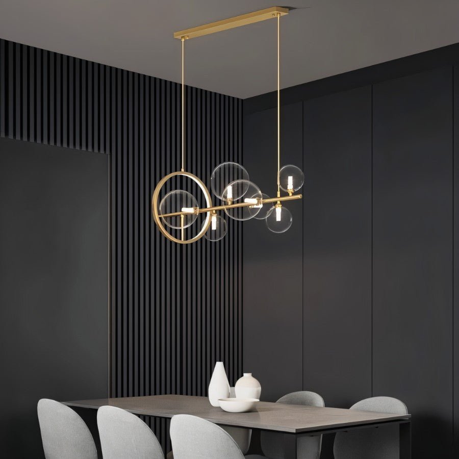 Clérachic gold bar chandelier seen at an angle, clear glass globes and a gold ring over a grey dining table and pale chairs.