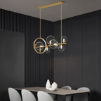 Clérachic gold bar chandelier seen at an angle, clear glass globes and a gold ring over a grey dining table and pale chairs.