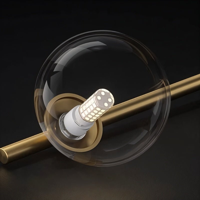 Clérachic close up of one clear glass globe on a brushed gold bar, with the white LED capsule bulb glowing inside.